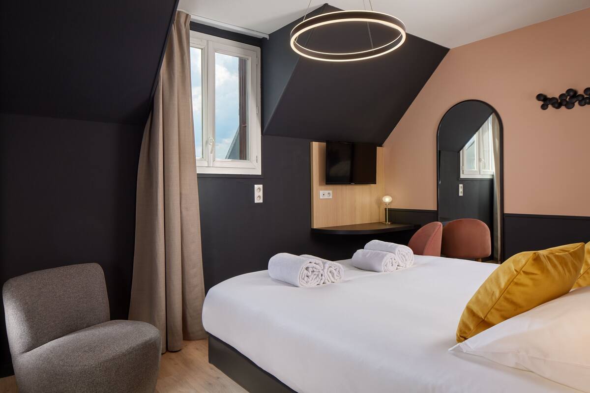 Une chambre d’hôtel moderne, équipée d’un lit, d’une chaise, d’un miroir et d’une fenêtre.