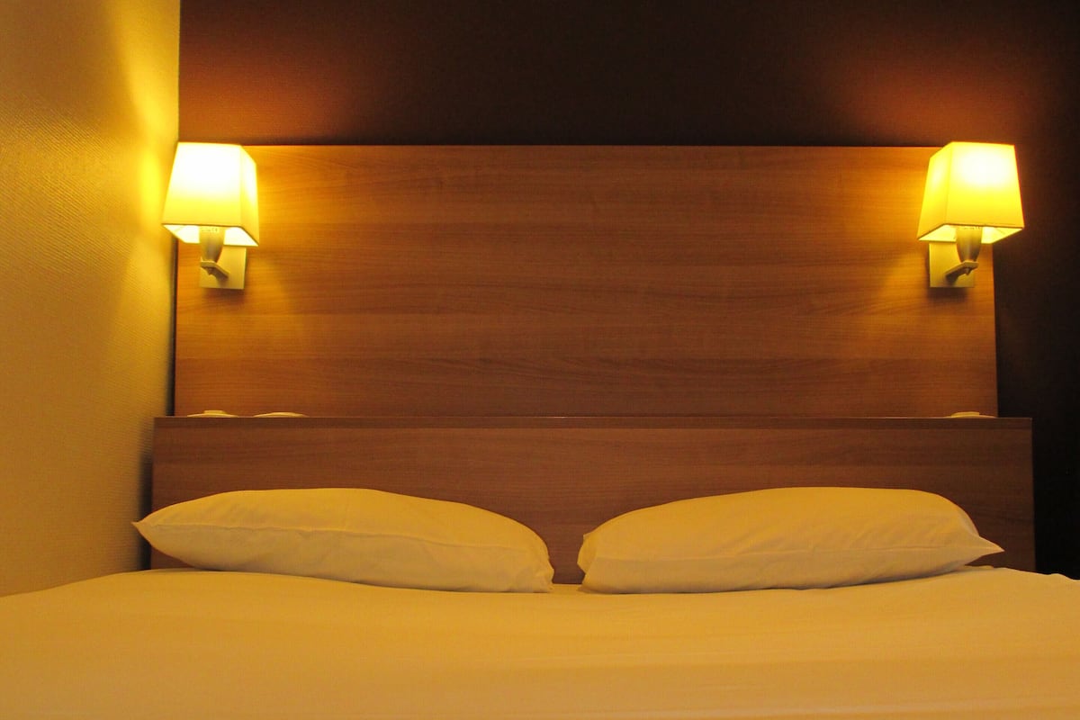 A neatly made bed with two pillows and two wall-mounted lamps on either side.