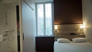 Una habitación de hotel moderna con una cama grande, ventana con vistas, zona de ducha y cabecero con luces empotradas.