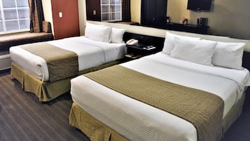 A hotel room with two beds, a bedside table with a phone, a TV on the wall, and a window with curtains.