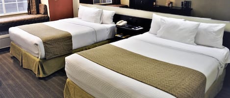 A hotel room with two beds, a bedside table with a phone, a TV on the wall, and a window with curtains.