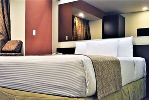 A hotel room with a large bed, a chair, a mirror, and a wardrobe. - Microtel Inn & Suites by Wyndham Toluca (Toluca)