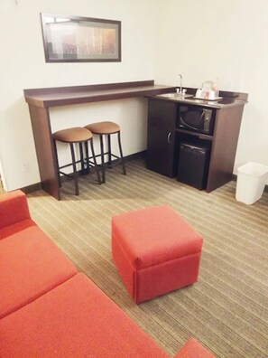 Une chambre d’hôtel compacte équipée d’une kitchenette, de deux tabourets, d’un four à micro-ondes et d’une petite poubelle.