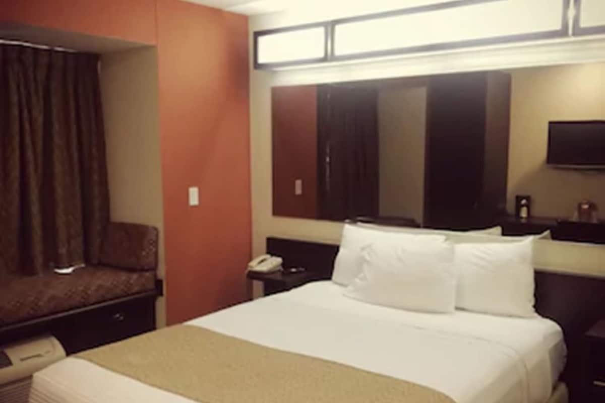 Una habitación de hotel con cama, escritorio, silla, televisor y espejo.