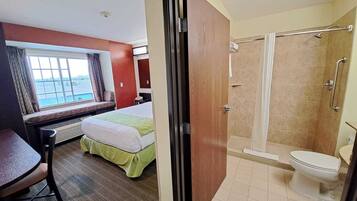 Una habitación de hotel con cama, escritorio, ventana con vistas, ducha y baño.