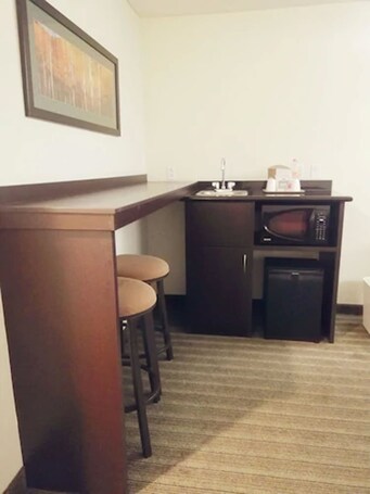 A compact kitchen with a microwave, sink, and small refrigerator. There are two stools at the bar counter.