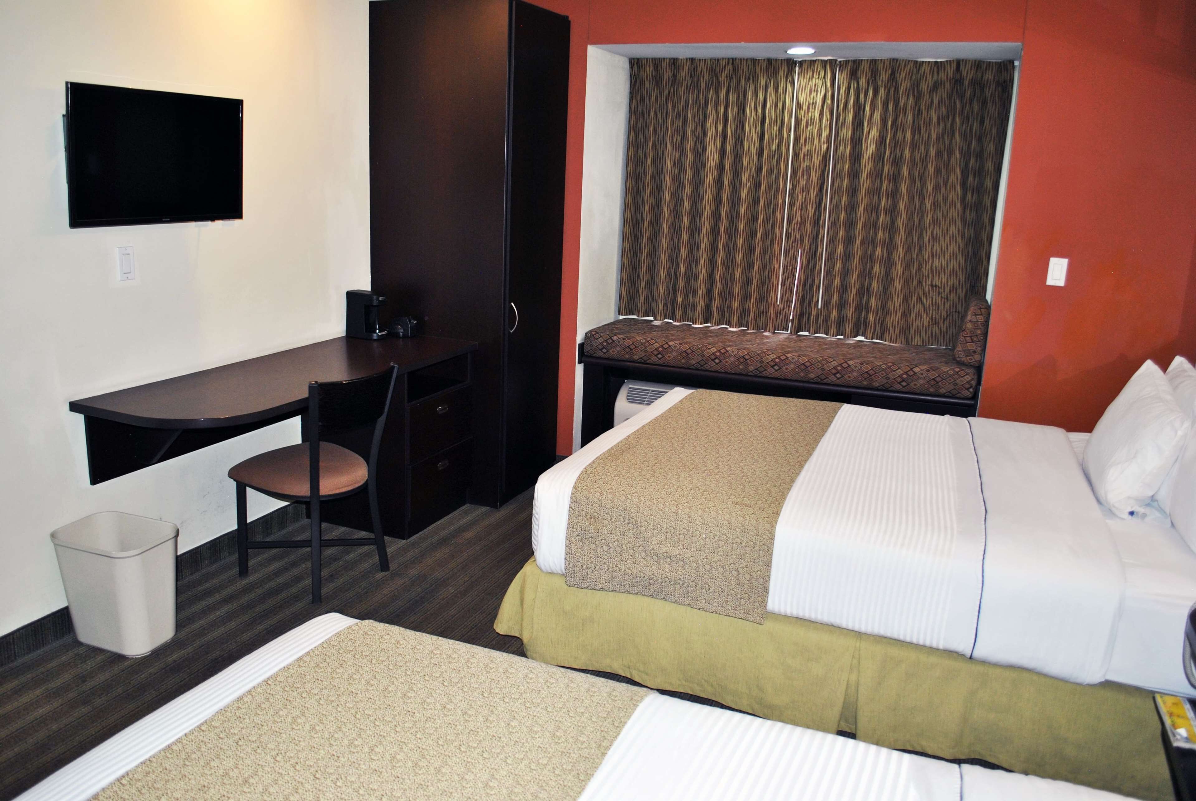 A hotel room with a bed, a desk, a chair, a TV, and a window with curtains.