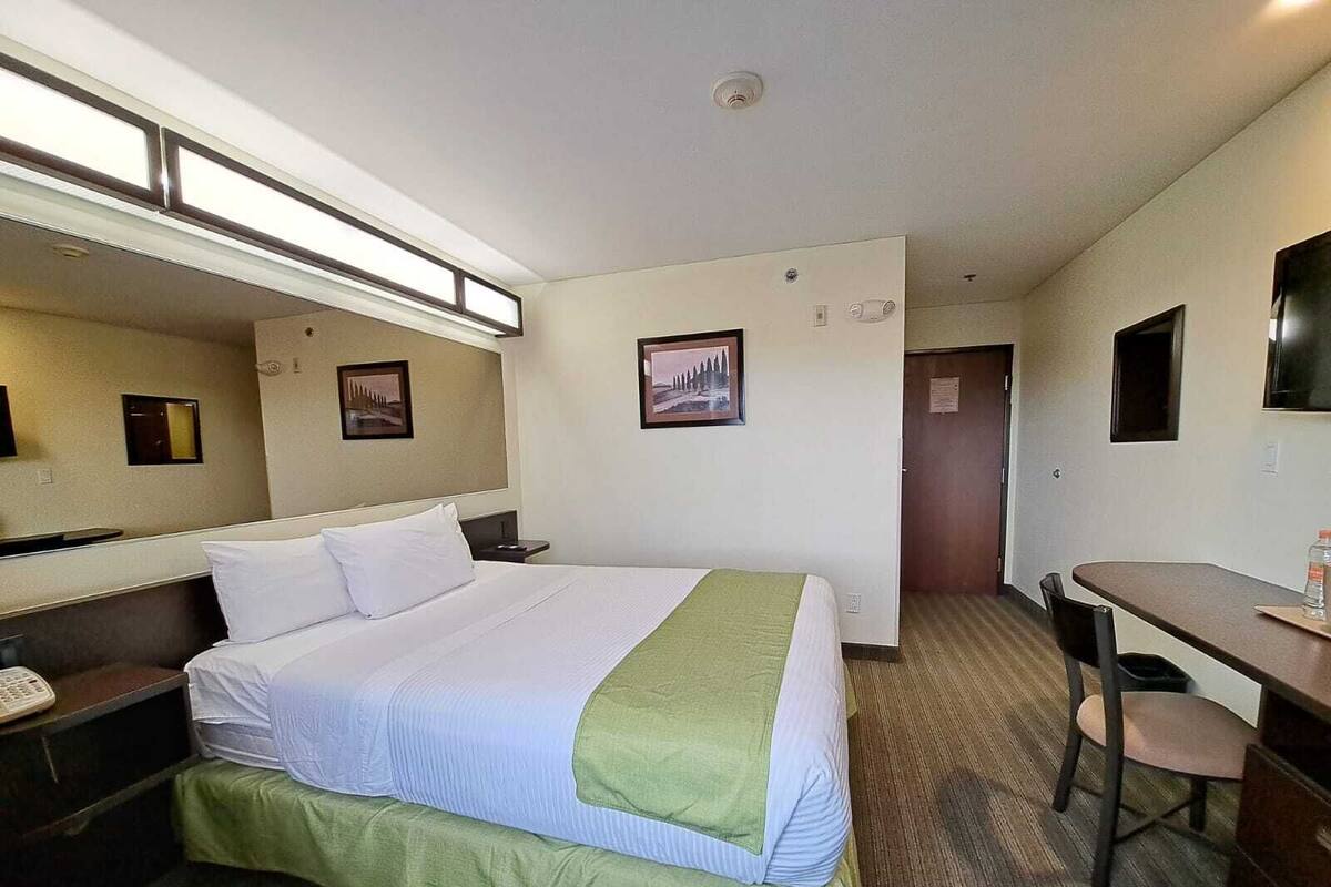 Habitación de hotel con cama, escritorio, silla, teléfono y un cuadro en la pared.