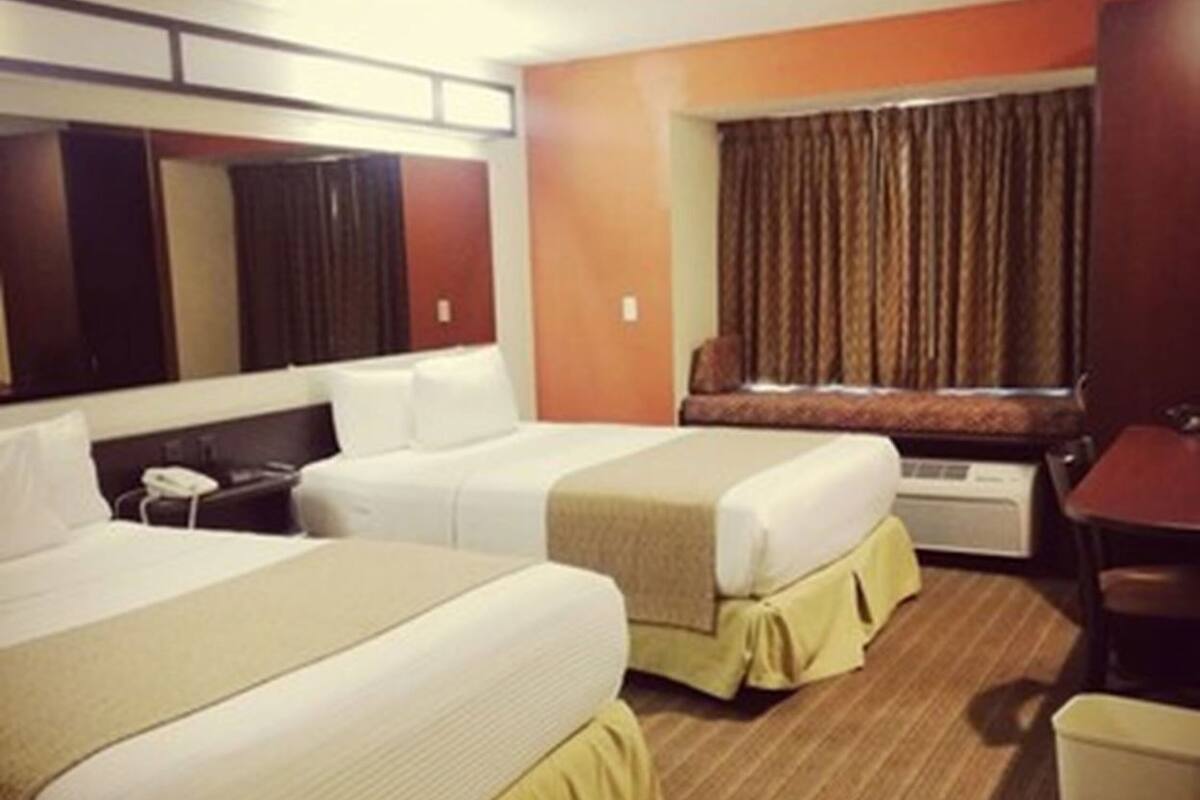 Habitación de hotel con dos camas, un escritorio, una silla, una ventana con cortinas y un televisor montado en la pared.