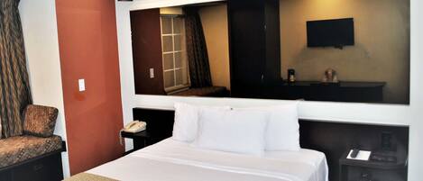 A hotel room with a large bed, a desk with a telephone, a TV mounted on the wall, and a window with curtains.