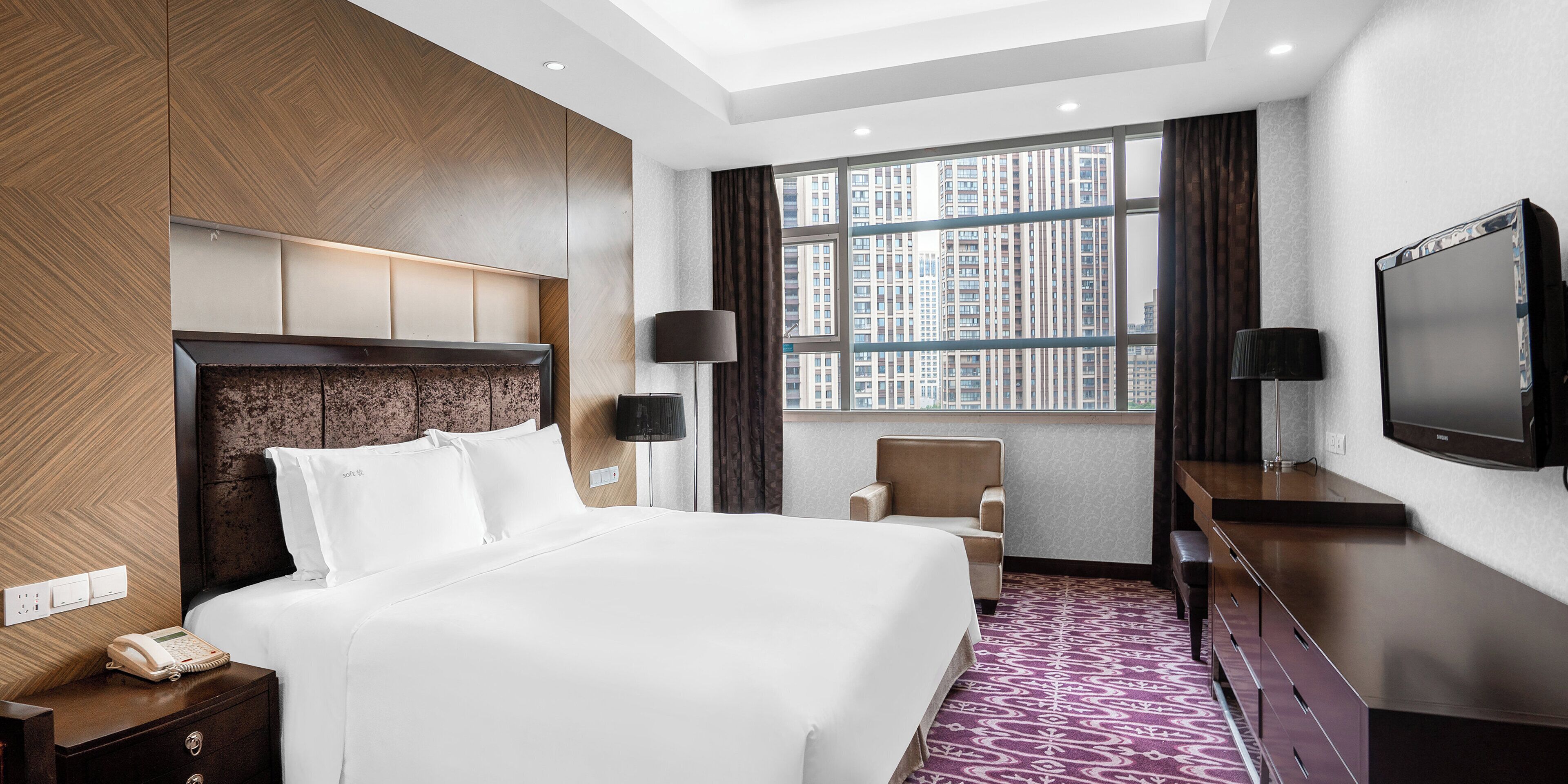 Une chambre d’hôtel avec un grand lit, un bureau, une chaise, une télévision et une fenêtre donnant sur la ville.