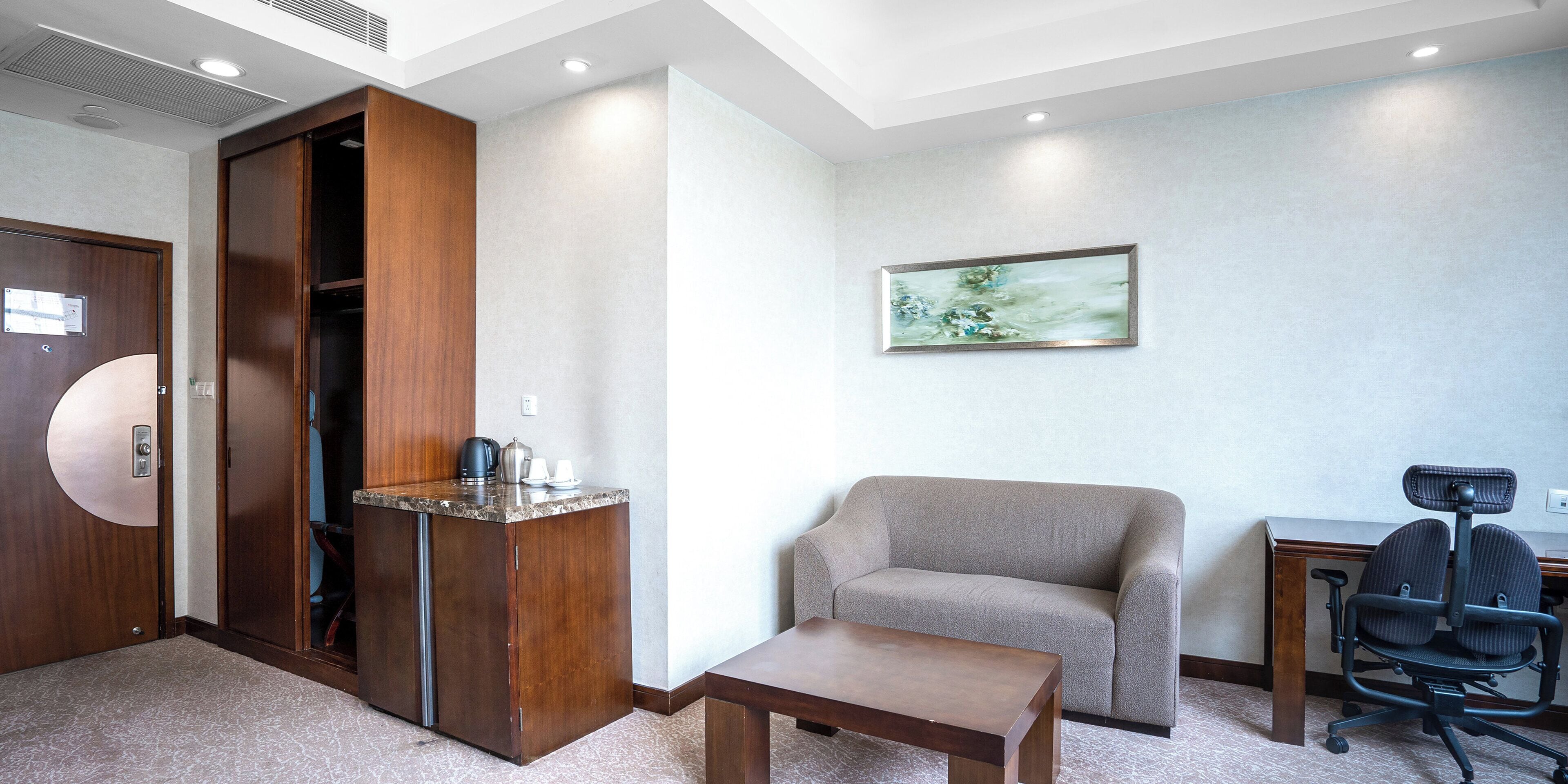 Una habitación de hotel con un armario de madera, un sofá gris, una mesita y un escritorio con una silla.