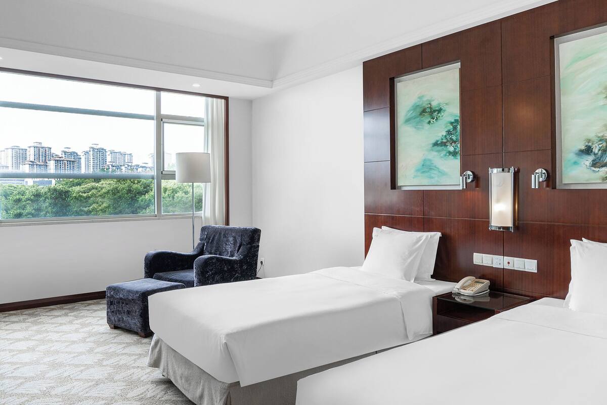A hotel room with two beds, a chair, a nightstand, and artwork on the wall.