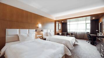 A hotel room with two beds, a desk, a chair, a desk lamp, and a large window with curtains.