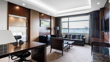 Una habitación de hotel moderna con escritorio, silla de oficina, sofá y un amplio ventanal con vistas a la ciudad.