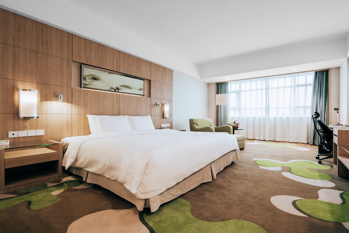 A hotel room with a large bed, a desk, a chair, a desk lamp, and a window with curtains.