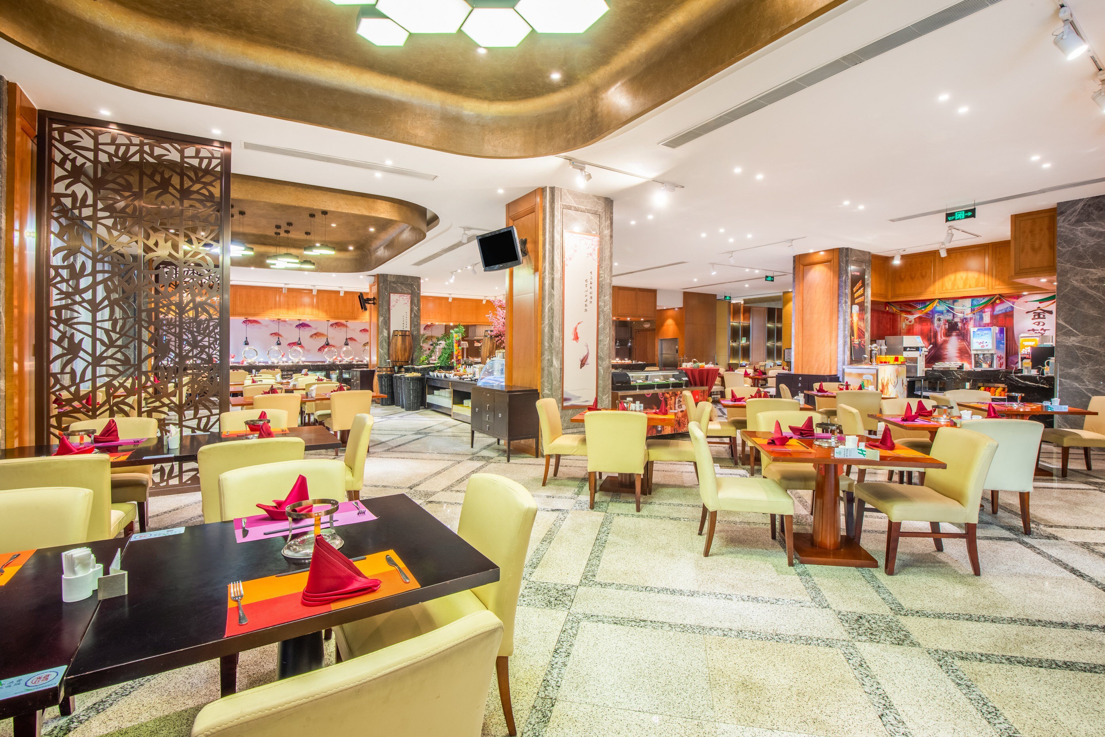 A spacious restaurant with multiple dining tables and chairs, a decorative wall, and a television screen.