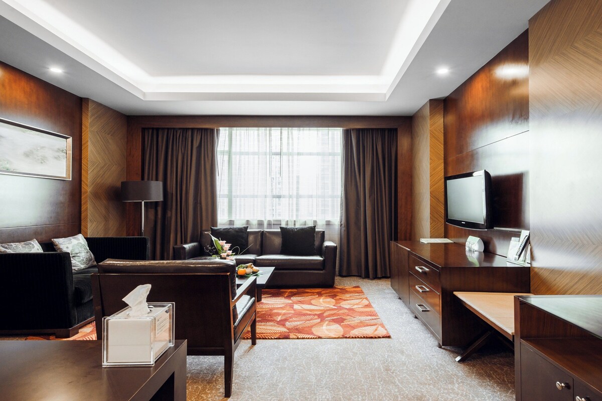 A modern hotel room with a sofa, a coffee table, a TV, and a desk.