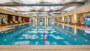 A large indoor swimming pool with a modern ceiling design, multiple lounge areas with chairs, and a clear pool lane divider. - Holiday Inn Changzhou Wujin by IHG (Changzhou)