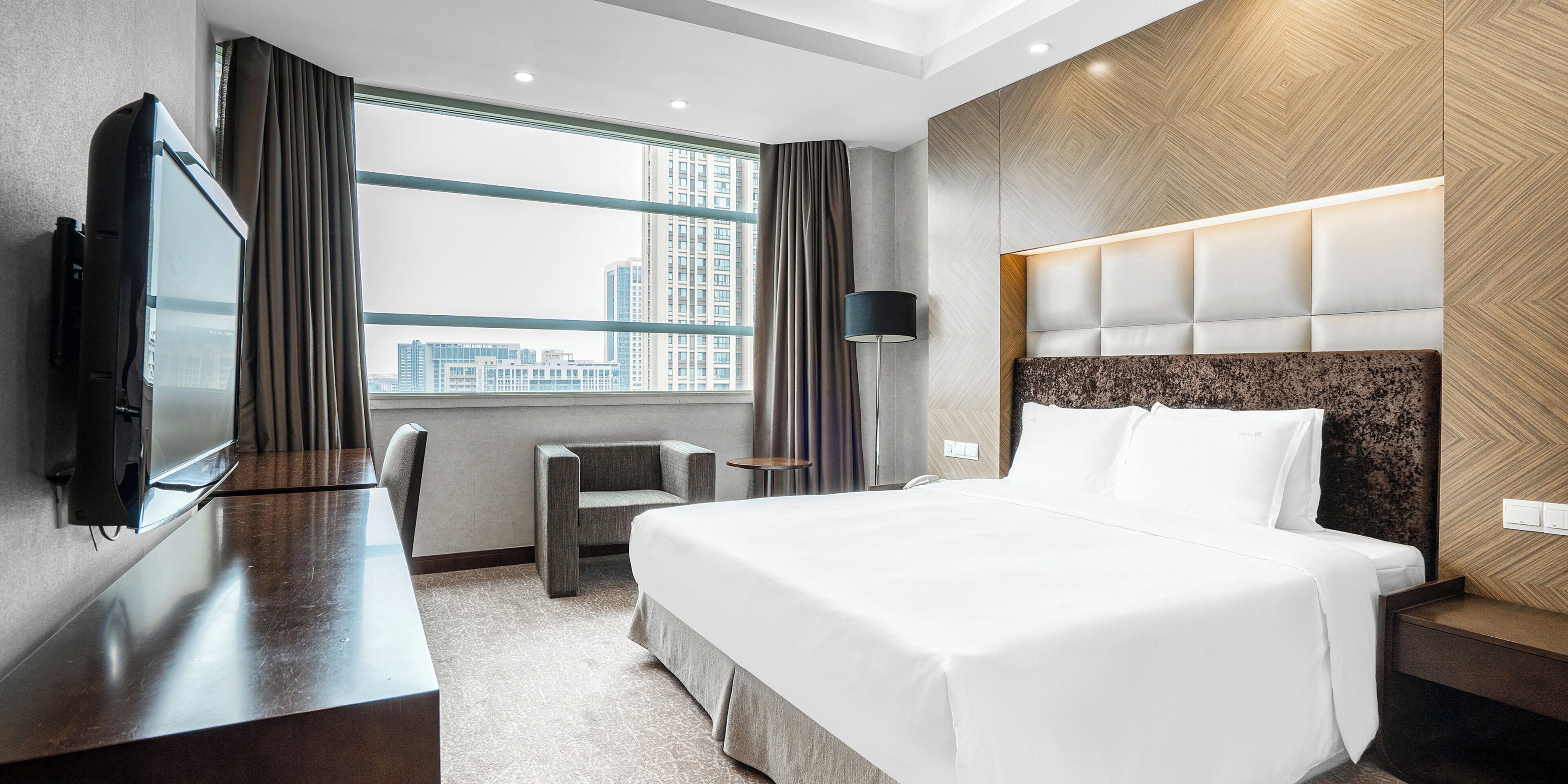 A hotel room with a bed, a desk, a chair, a TV, and a window with a city view.