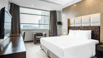 A hotel room with a bed, a desk, a chair, a TV, and a window with a city view.
