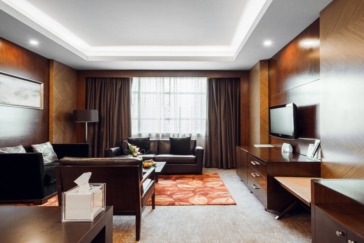 A modern hotel room with a sofa, a coffee table, a TV, and a desk.