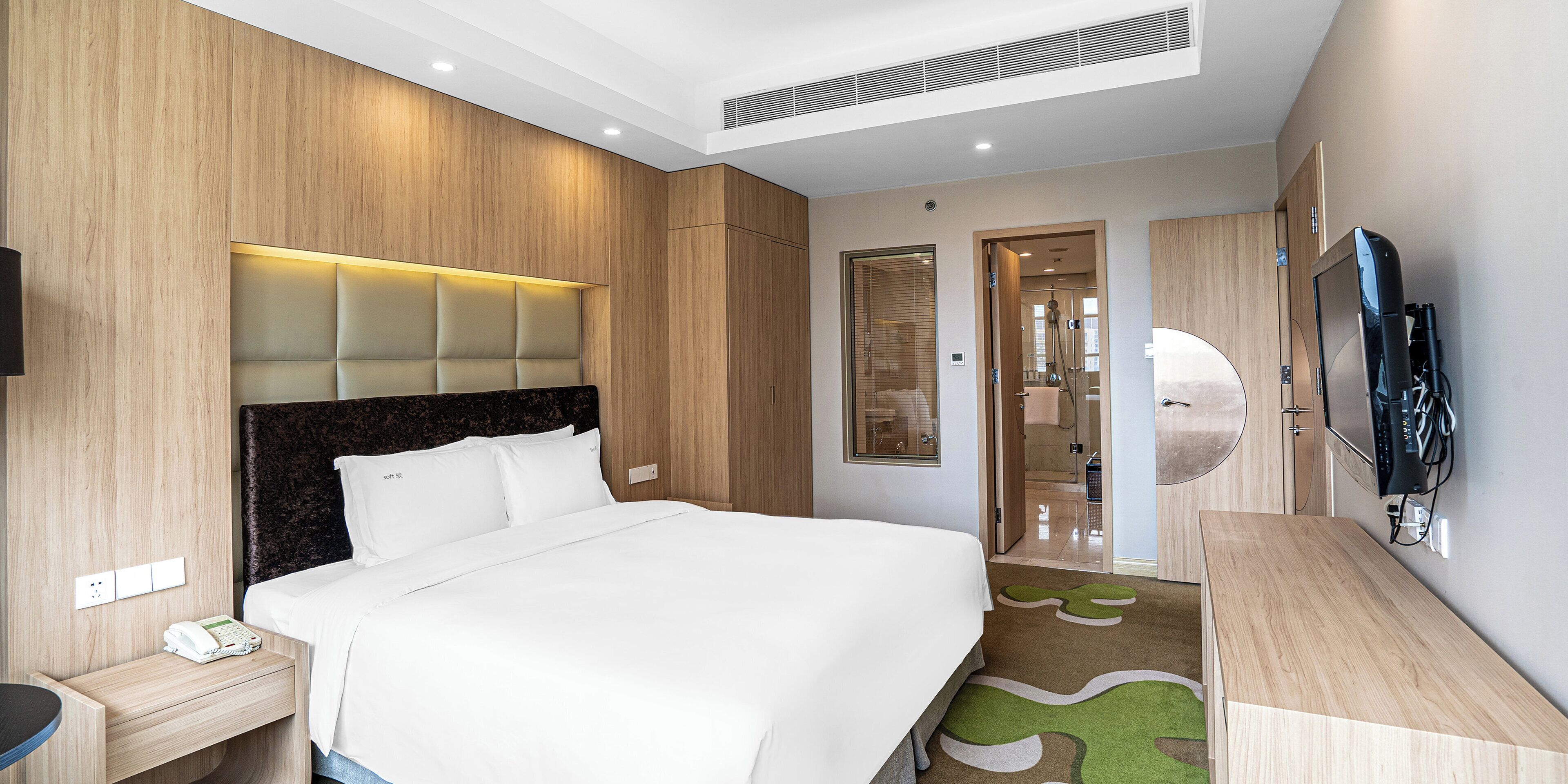 Camera d'albergo con un letto, una scrivania, un telefono, una televisione e un bagno visibile tramite una porta in vetro.