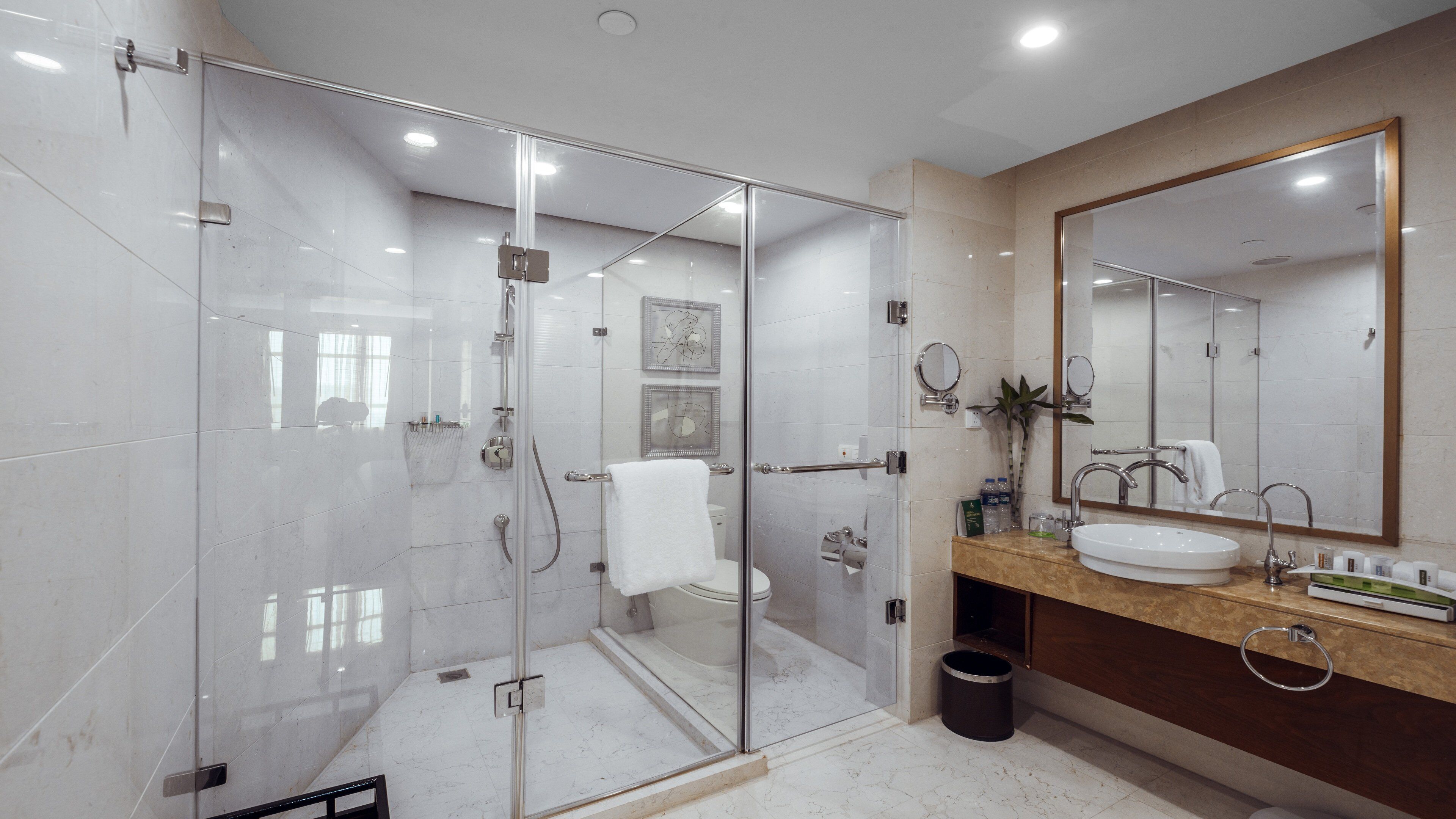 A modern bathroom with a glass-enclosed shower, a large mirror, and a marble-tiled floor.