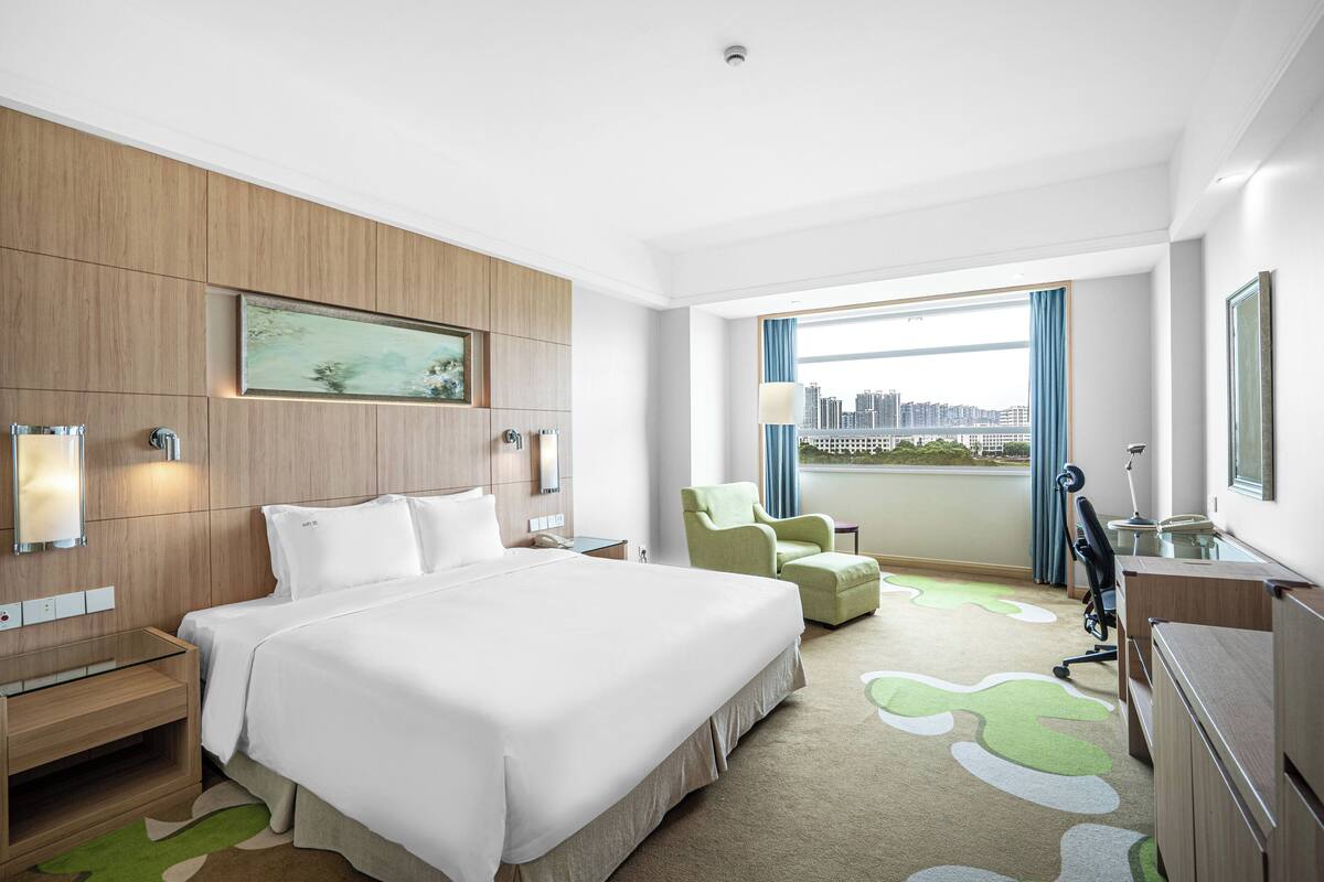 A hotel room with a large bed, a desk, a chair, and a view of the city.