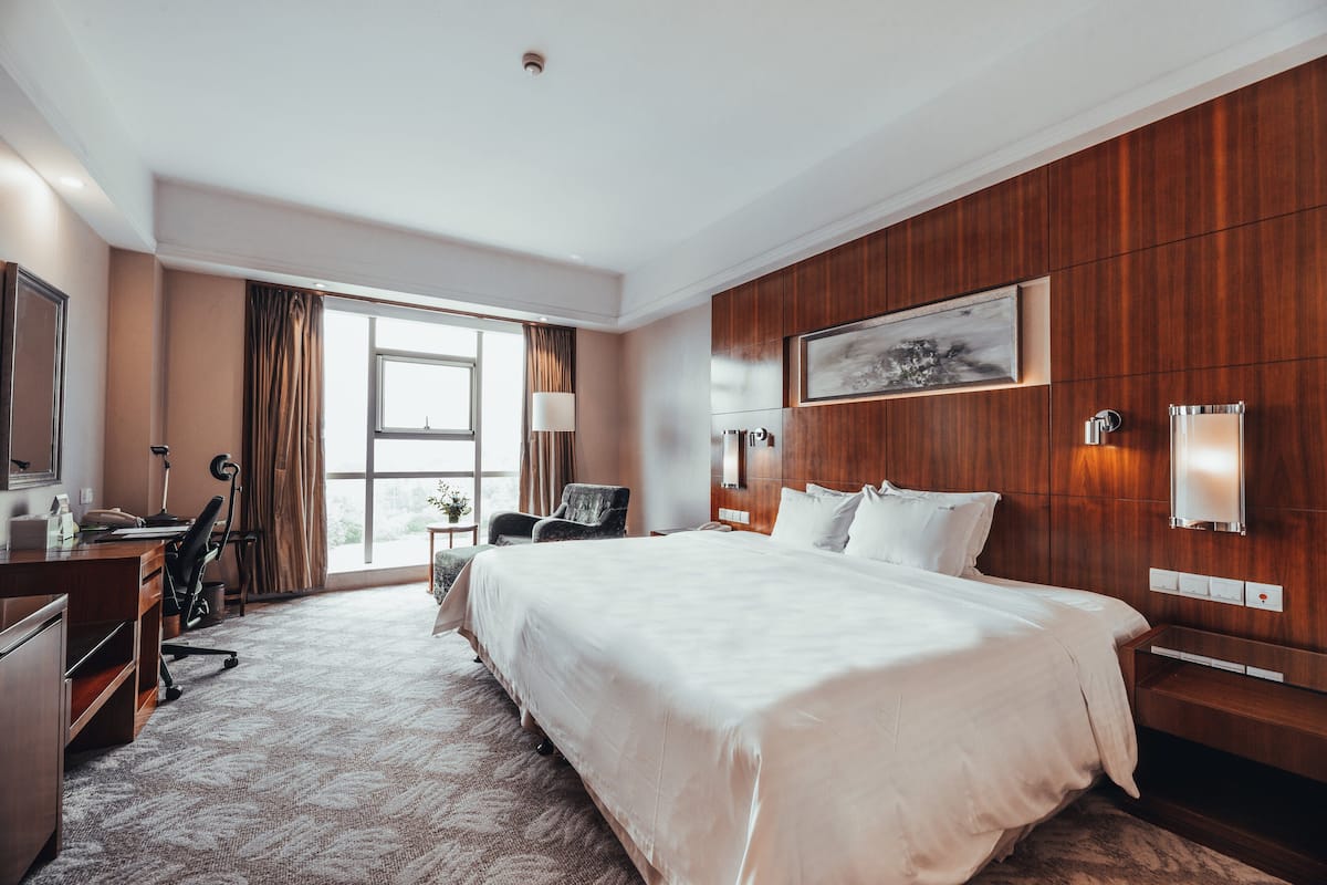 A hotel room with a large bed, a desk, a chair, a lamp, and a window with curtains.