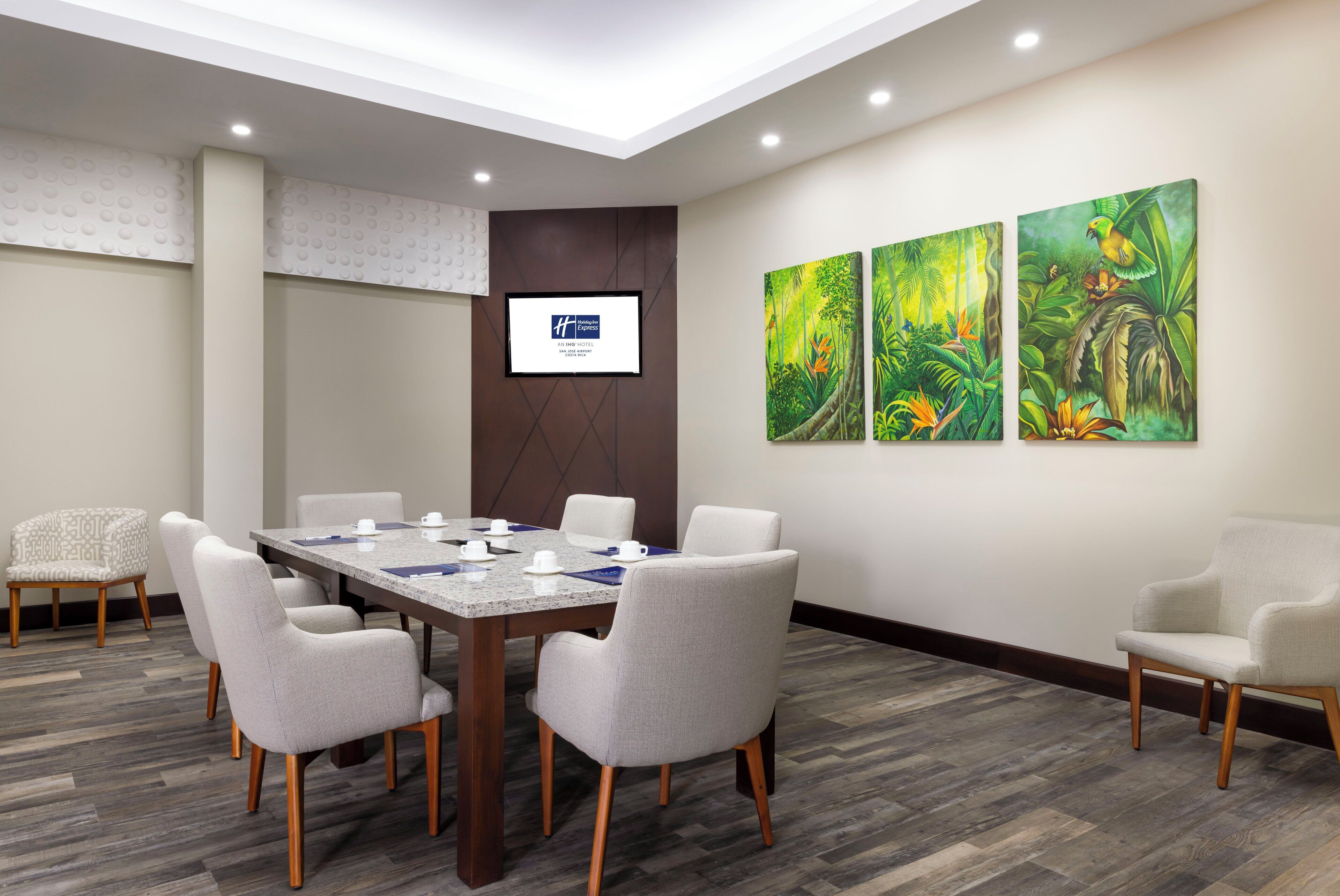 A conference room with a long table, six chairs, and a screen on the wall.