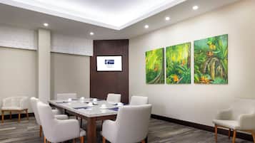 A conference room with a long table, six chairs, and a screen on the wall.