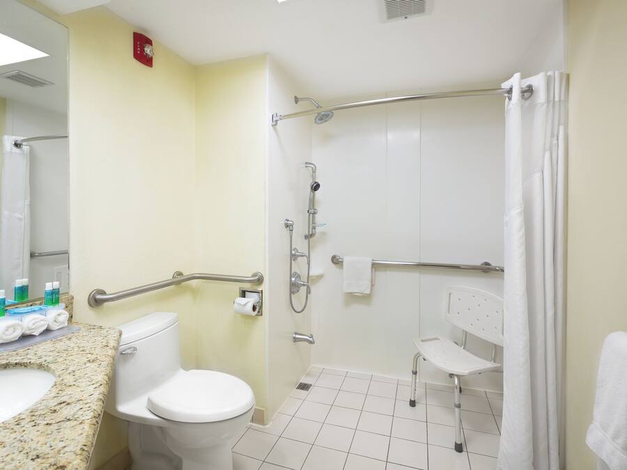 Baño con inodoro, lavamanos, ducha y barras de apoyo.