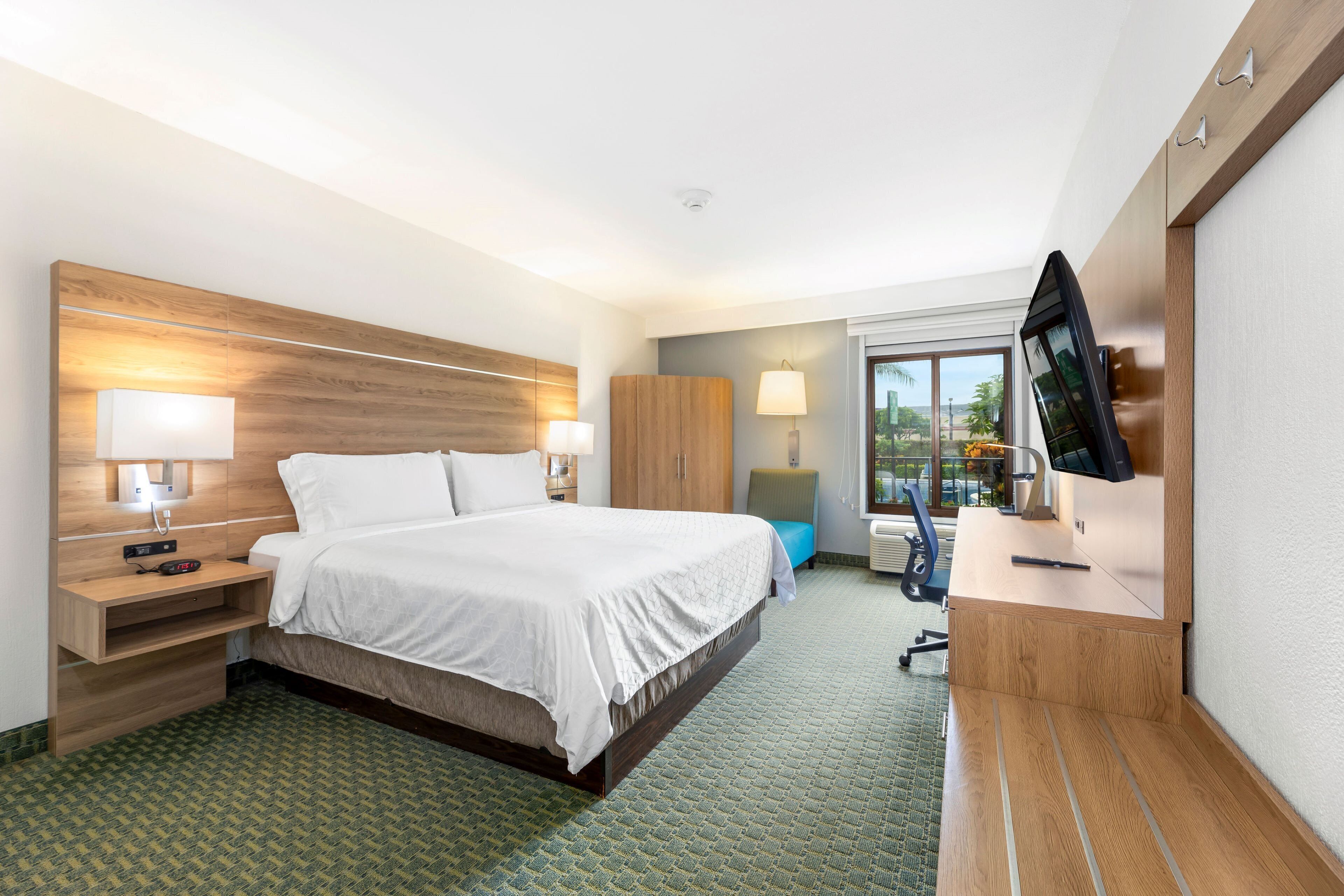 A hotel room with a large bed, bedside lamps, a desk with a flat-screen TV, and a wardrobe.