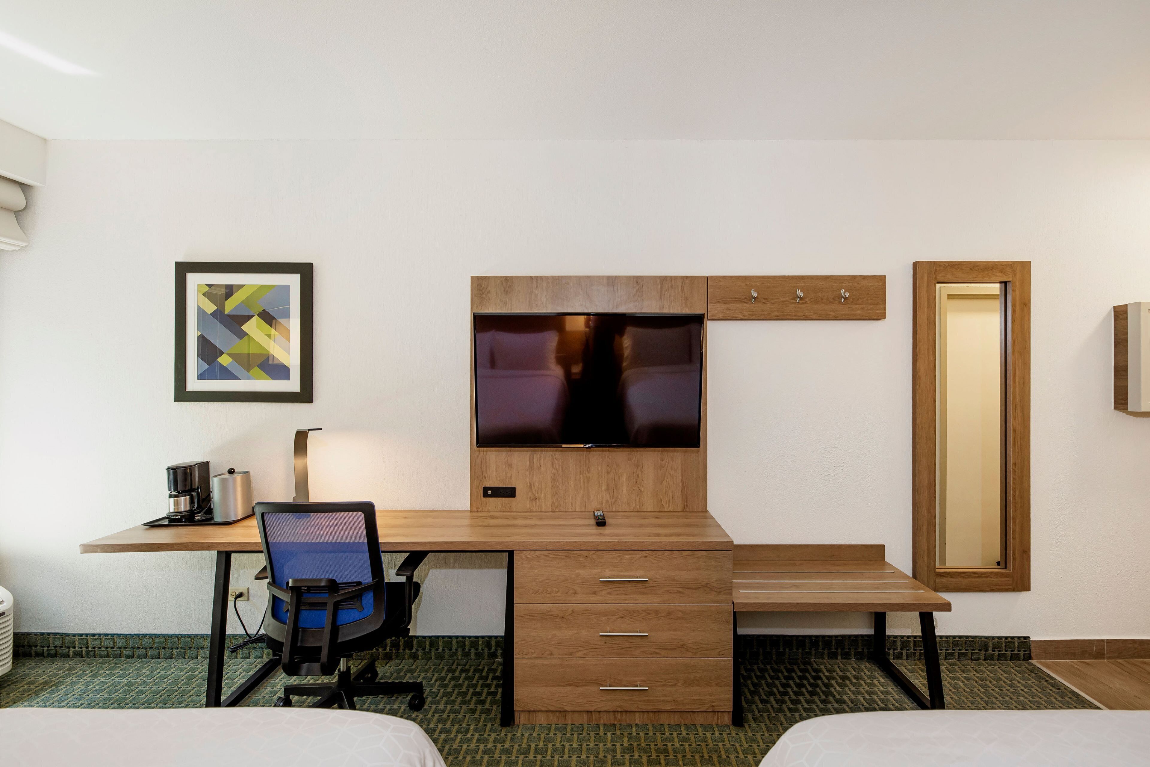 Ein Hotelzimmer mit Schreibtisch aus Holz, einem Sessel, einem Bett, einem Fernseher und einem gerahmten Bild an der Wand.