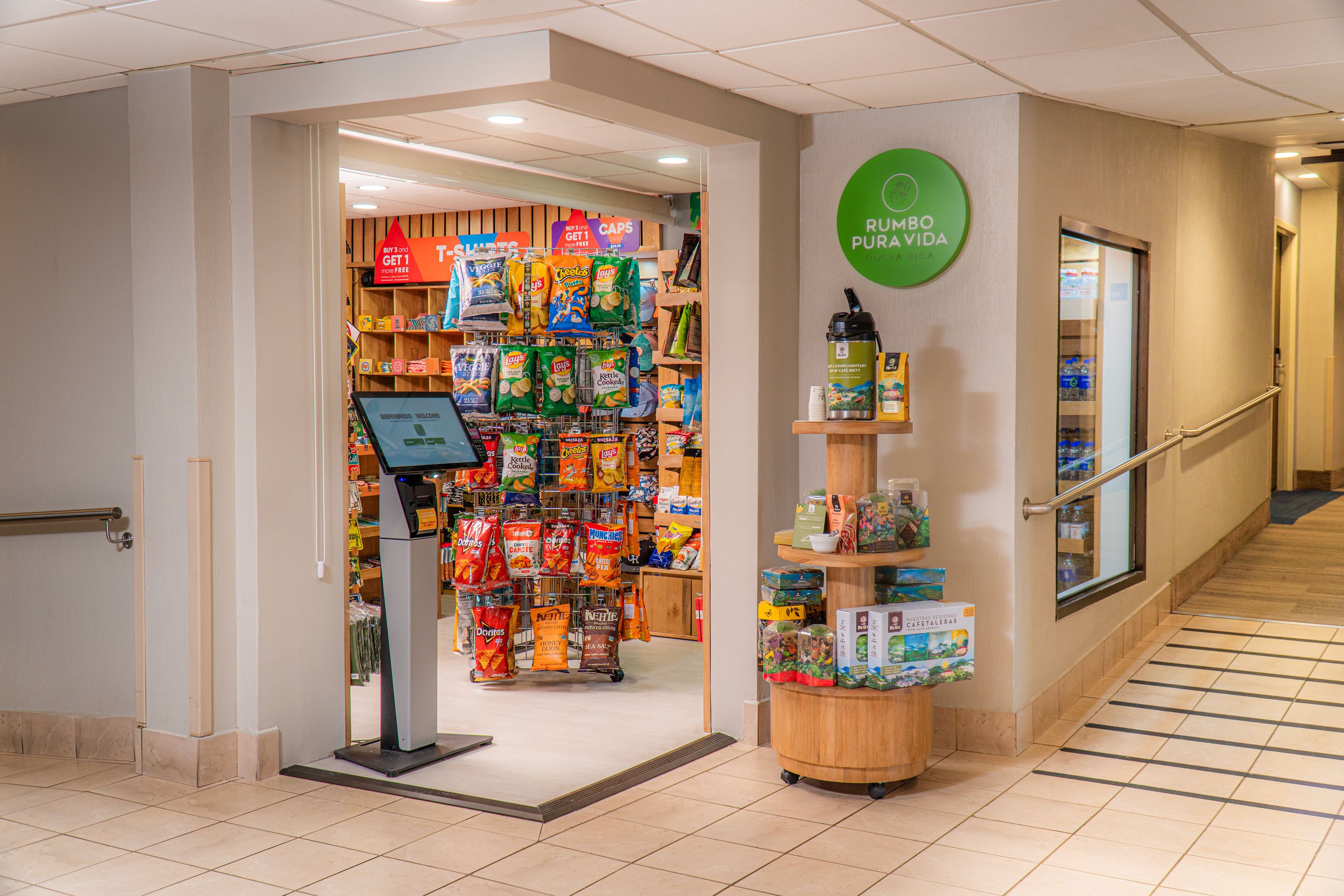 A grocery store entrance with a self-checkout kiosk and a variety of snacks and beverages on display.