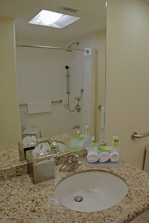 Un bagno con lavandino, specchio, porta asciugamani, doccia e articoli da toilette.
