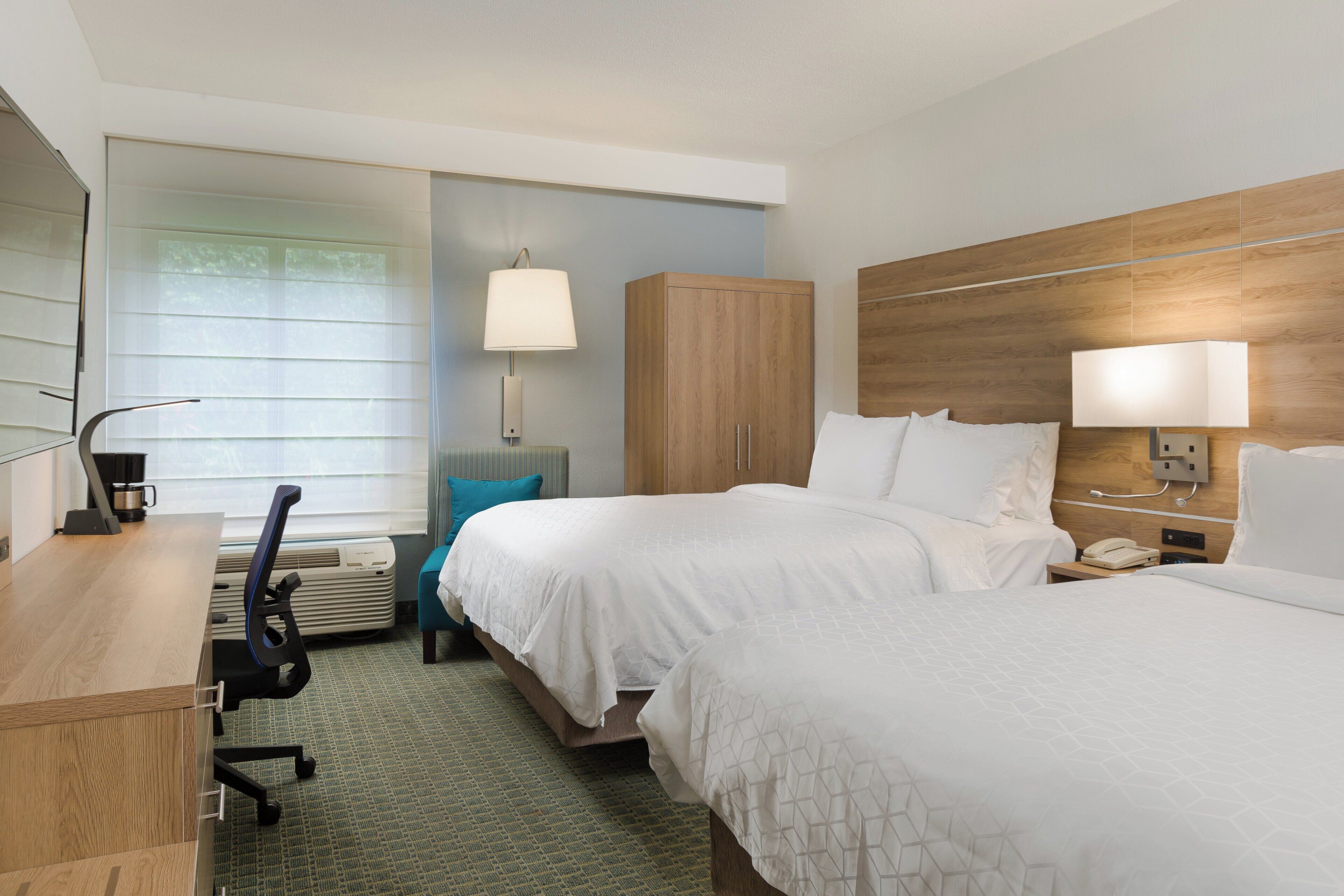 A hotel room with two beds, a desk, a chair, a lamp, and a wardrobe.