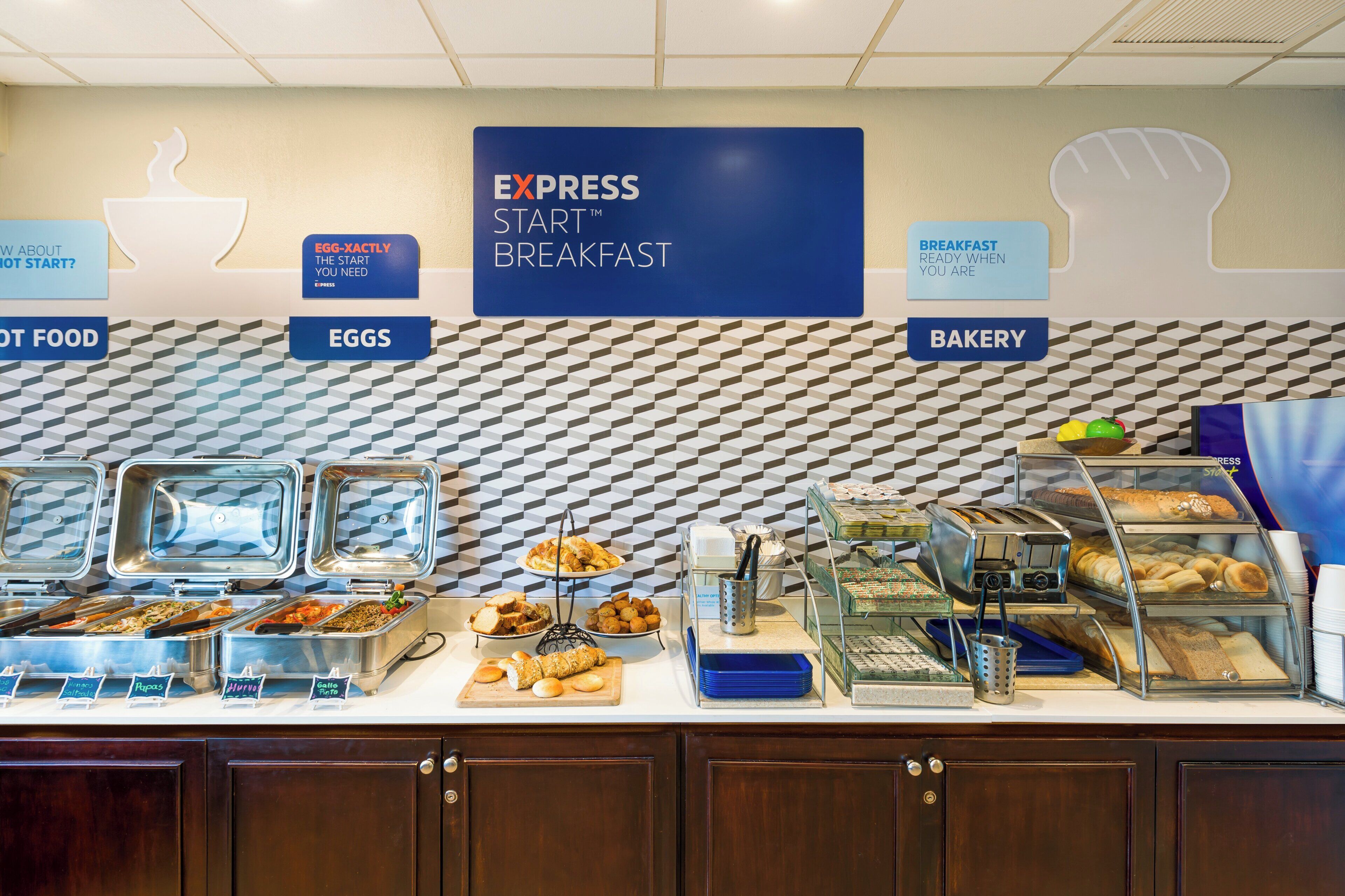 A breakfast buffet area with labeled sections for eggs, hot food, and bakery items.
