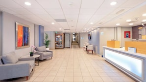 A hotel reception area with a reception desk, seating area with sofas, a framed artwork on the wall, and a store named "SUNDRY SHOP" in the background. - Holiday Inn Express San Jose Costa Rica Airport by IHG (Rio Segundo)