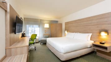 A hotel room with a large bed, a desk with a chair, a TV mounted on the wall, and a lamp on the nightstand.