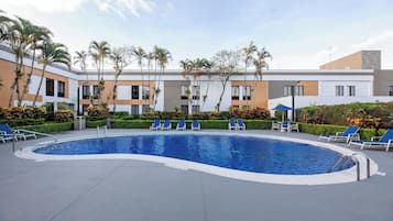 A swimming pool with blue water, surrounded by lounge chairs and palm trees.