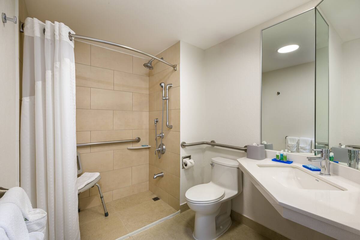 A bathroom with a shower, toilet, and sink, equipped with grab bars and a wheelchair-accessible shower chair.