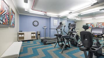 A fitness room with exercise equipment, a clock, and informational posters on the walls.