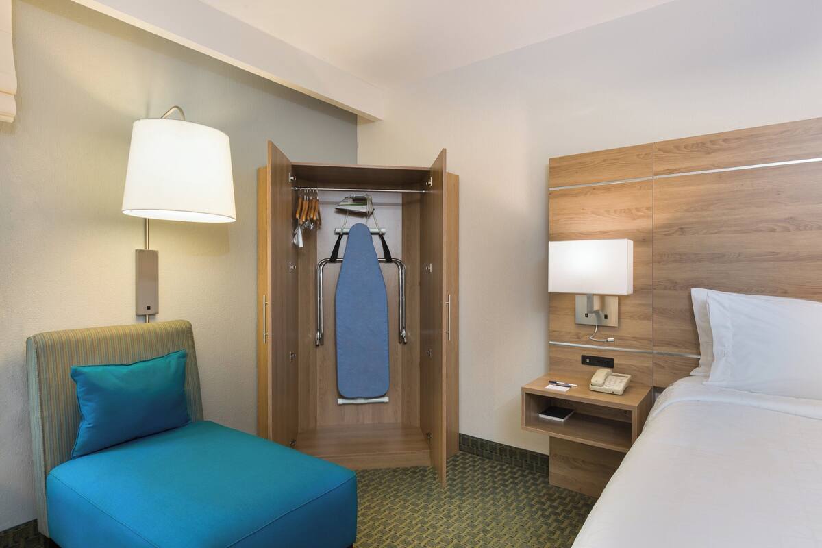 A hotel room with a bed, a desk with a telephone, a chair with a cushion, a wardrobe, and a hanging garment.\n\nVerification: The room layout, bed, desk with a telephone, chair with a cushion, wardrobe, and hanging garment are all clearly visible and identifiable.