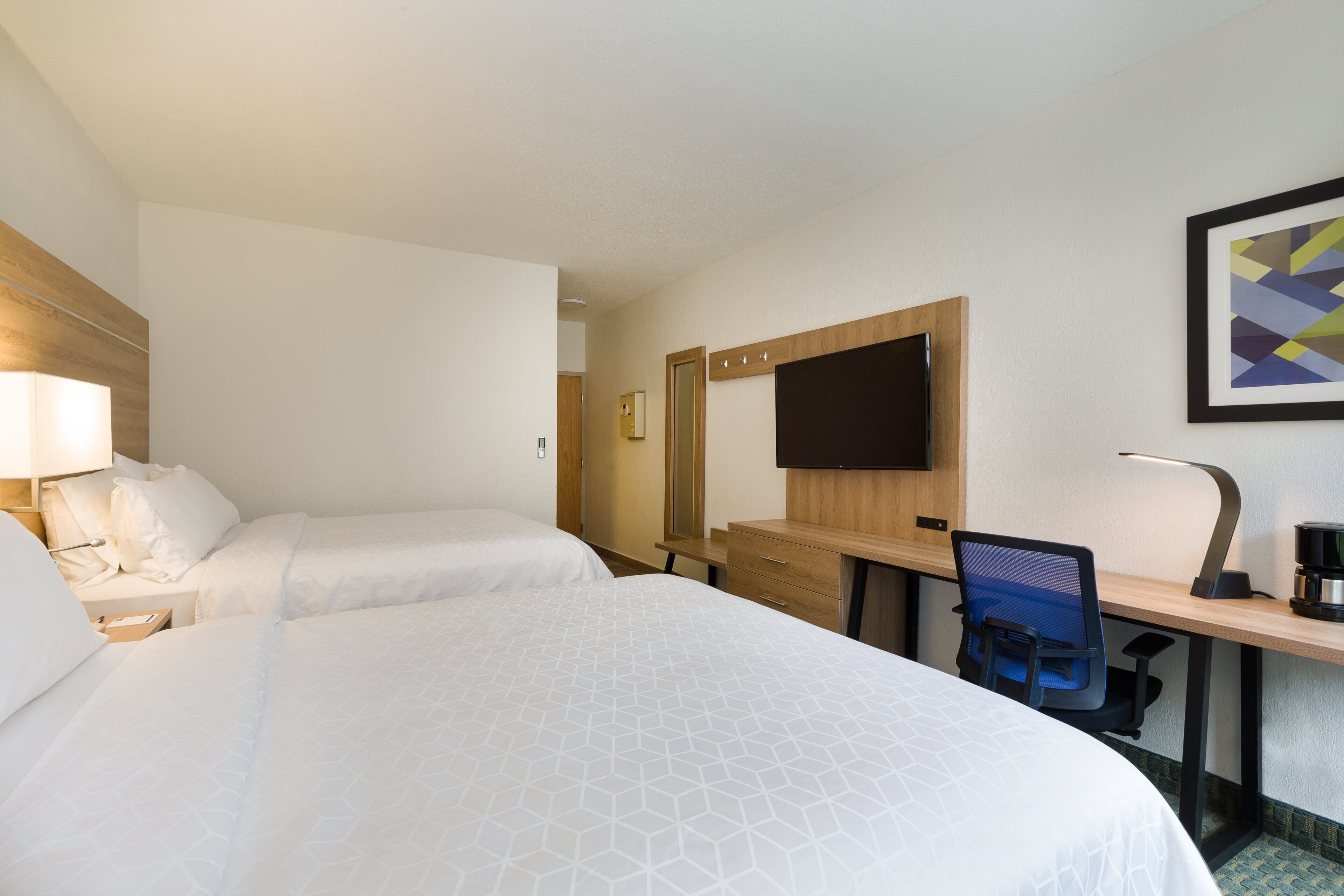 Une chambre d’hôtel avec deux lits, un bureau, une chaise, une télévision et une machine à café.