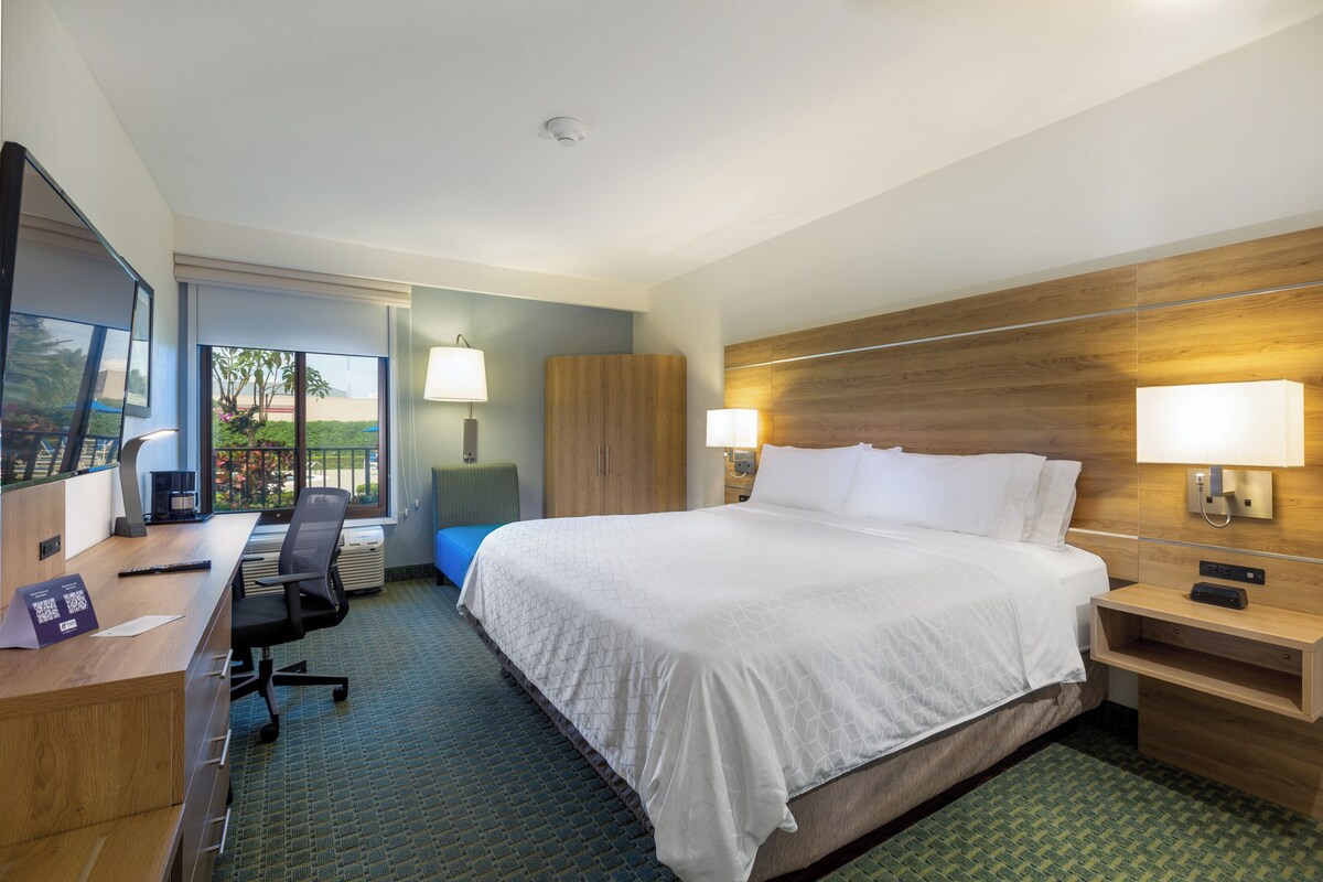 A hotel room with a large bed, a desk with a chair, a wardrobe, and a TV.