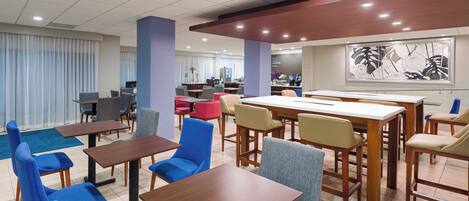 A hotel dining area with multiple tables and chairs, a coffee station, and a large abstract art piece on the wall.