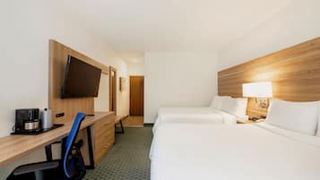 A hotel room with a wooden desk, a television, a bed, and a nightstand with a lamp.