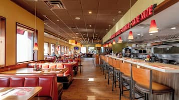 A restaurant with booths and high-top tables, a bar area, and a kitchen visible in the background.